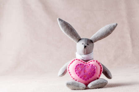 Needlework hobby concept. Handmade bunny with soft heart on soft backgroundの写真素材
