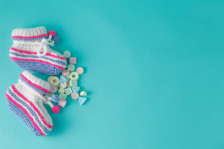 Newborn announcement concept. Knitted booties on aquamarine background with sweetsの写真素材