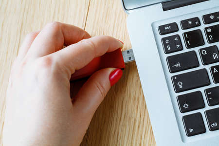 Close up of a woman hand plugging a red pendrive on a laptop