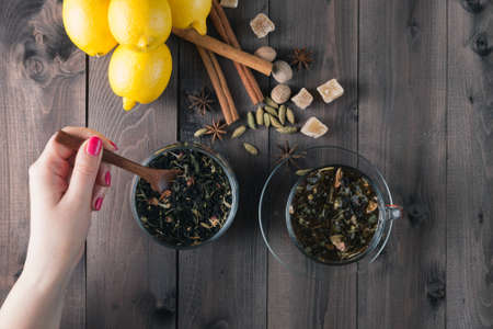 Woman mixing spoon herbal tea in glass jar on rustic wooden table
