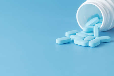 Blue pills an pill bottle on blue background