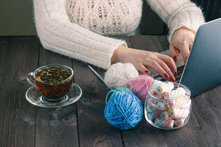 woman is knitting in front of laptop. She is teaching on-line learners the art of knitting