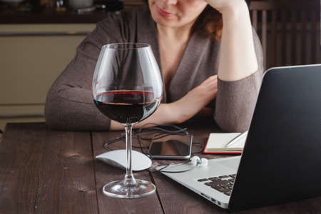 woman working from home on a laptop enjoying a glass of wineの写真素材