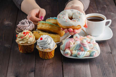 Woman give sweet donut. Coffee and marshmallow on rustic wooden table.の写真素材