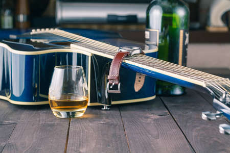 Guitar side view, strings and fingerboard with glass of alcohol on tableの写真素材