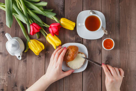 Holiday breakfast with flowers, woman buttering breadの写真素材