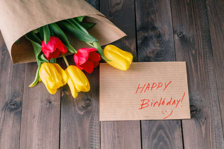 Tulip bouquet in craft paper on wooden table, message happy birhdayの写真素材