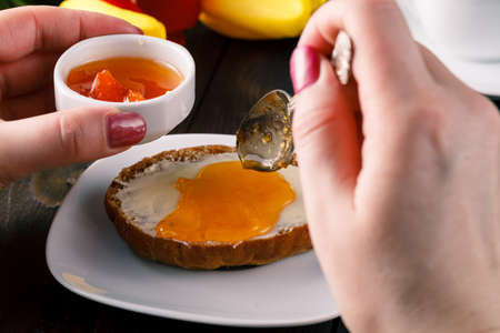 Breakfast concept. Woman take jam on buttering bread with tulips on tableの写真素材