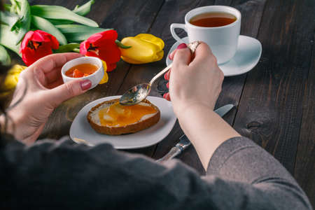 Breakfast concept. Woman take jam on buttering bread with tulips on tableの写真素材