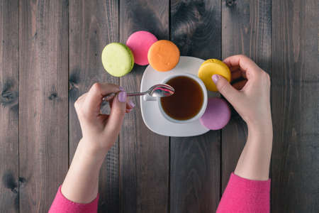 Female hand with tasty colorful macaroons on dark wooden backgroundの写真素材