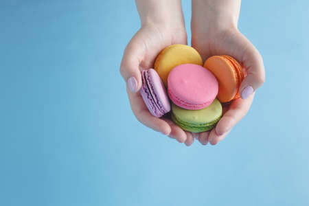 Female hands holding colorful french macaroonsの写真素材