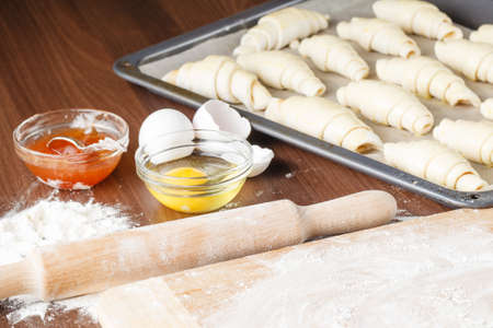 Raw croissants on parchment preparation process, rolling pin, eggs, yolk and flour