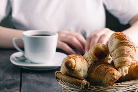 Basket with tasty fresh croissants and hot morning cup of coffee or tea with female working at...