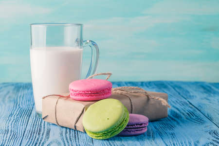 Assortment of gentle colorful macaroons and glass with milk on color wooden background with gift boxの写真素材