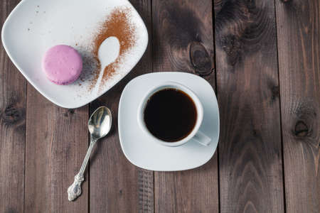 white cup of espresso coffee with colourful French macaroon on dark rustic wooden background