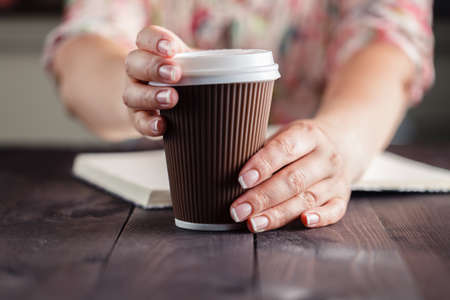 Woman holding takeout coffee at table and opening cupの写真素材
