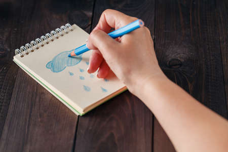 Woman drawing blue rain in notebook.の写真素材