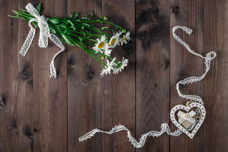 flat lay of daisies forming a frame on a dark wooden background with heart symbol