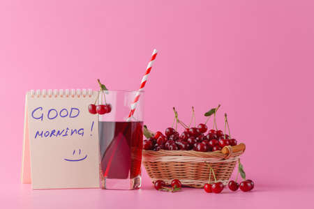 Sweet cherries in a basket and glass of juice on pink  background with message good morningの写真素材