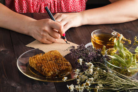 Woman write recipe of herbal tea. Cup of herbal tea with linden flowers on a old wooden backgroundの写真素材
