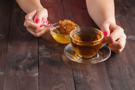 Woman hold cup of hot tea in glass cup, jar of honey, honey dipper on the old wooden backgroundの写真素材