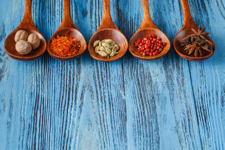 Collection of spices on wooden spoons and a blue wooden table