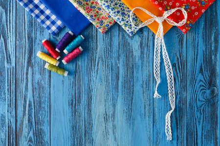 cotton fabrics for sewing, lace and accessories for needlework on wooden background. Spool of...