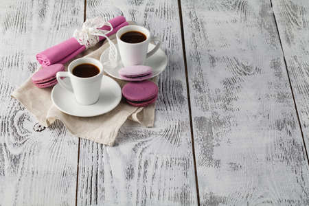 Two cups of freshly brewed espresso coffee with macaroons on a textured wooden table top with copyspaceの写真素材