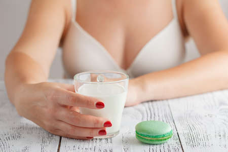 glass of milk held in a woman's hand. Fresh milk and macaroon cookies on wooden tableの写真素材