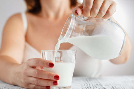 Womans hand pouring milk from a jug in a glassの写真素材