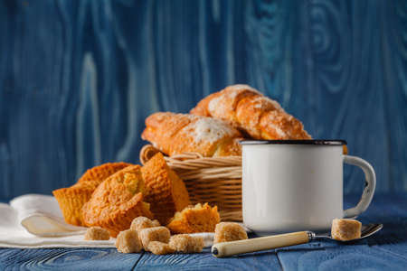 cup of black coffee in an old enamel mug, breakfast croissants on background, vintage rustic table
