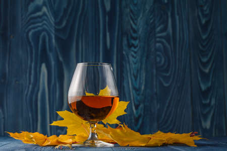 Cognac glass with dried autumn leaves on the tableの写真素材