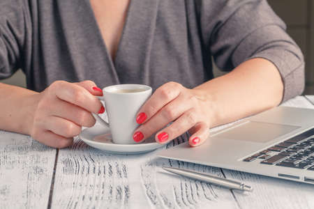 adult single female sitting at table holding coffee cup and typing on laptop with light flare coming through windowの写真素材