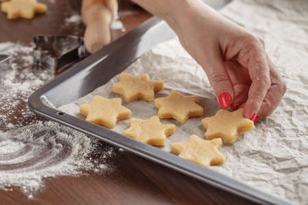 Homemade baking, kitchen scene showing  woman holding baking tray with cut shortbread biscuits on baking paper ready to be cooked.の写真素材