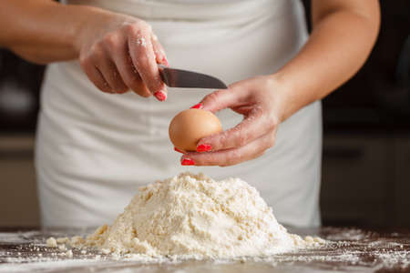 male hands break the egg into flour for pasta on old wooden kitchen table.