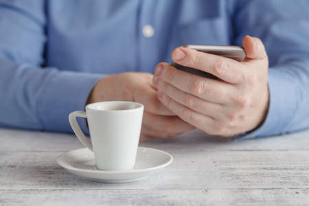 Man sits with smartphone at table with cup of coffeeの写真素材