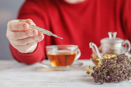 Male looks the temperature on the thermometer and drinking herbal tea with honeyの写真素材