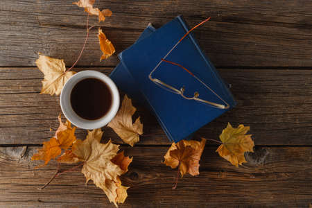Cup of coffee with an old book and oak leaves. On wooden background.の写真素材