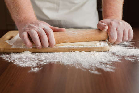 Men hands roll out dough close up. Man preparing dough for cooking pasta on a wooden tableの写真素材