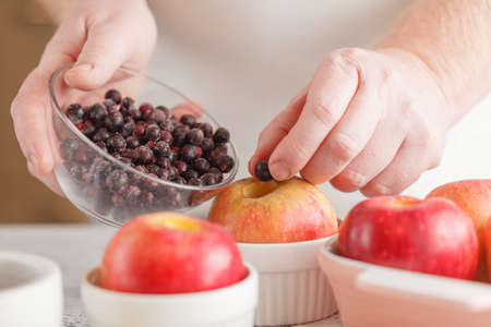 man cooking baked apple with berries in modern kitchen with wooden tableの写真素材