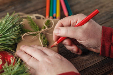 Male hand wrapped Christmas gift in the paper on dark wooden table, top viewの写真素材