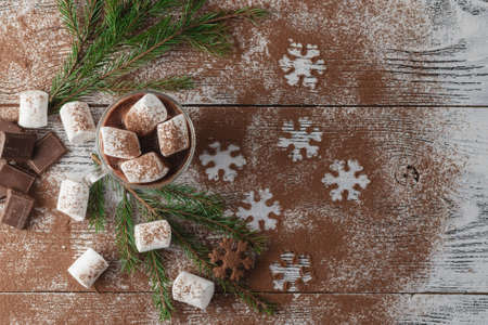 Winter hot cocoa with marshmallows, chocolate syrup, sugar snowflakes in a tall glass on a wooden background.の写真素材