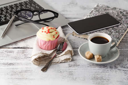 Coffee cup and muffin on table with computerの写真素材