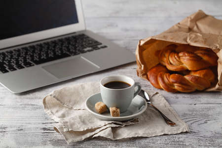 Fresh pastry and cup of brew coffee on table in office with laptopの写真素材
