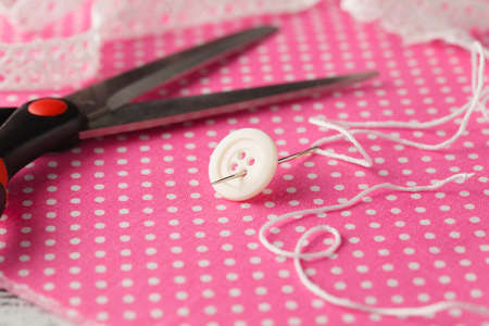 Needle and button on pink polka dot clot