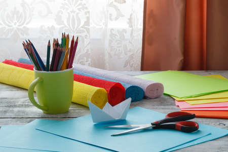 Set of origami boats and square sheets of colored paper on a wooden table. How to make a simple origami ship. Paper folding tutorial. Kids art and craft projectの写真素材