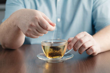 man brewing tea bag with glass of tea on tableの写真素材
