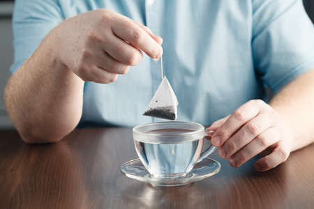 man brewing tea bag with glass of tea on tableの写真素材