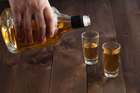 Pouring alcohol in shot glass on wooden tableの写真素材