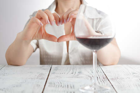 Love to wine. Female hold hands in heart sign against wine glassの写真素材